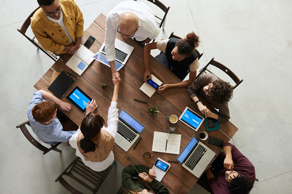 People shaking hands at a table full of laptops and tablets